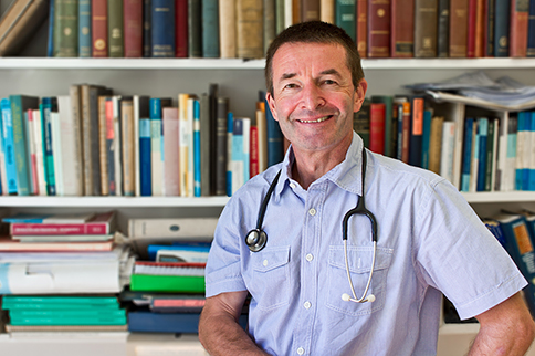 GP smiling in front of bookshelf