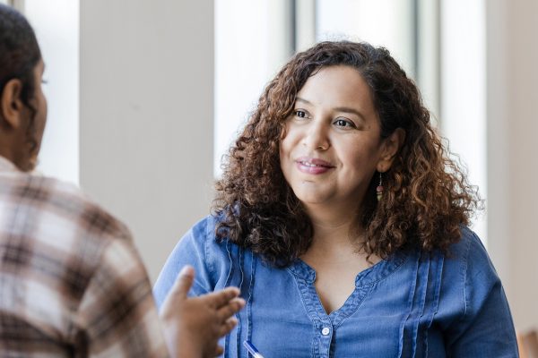 The mid adult female counselor listens with a smile to the unrecognizable emotionally distressed young adult female university student.